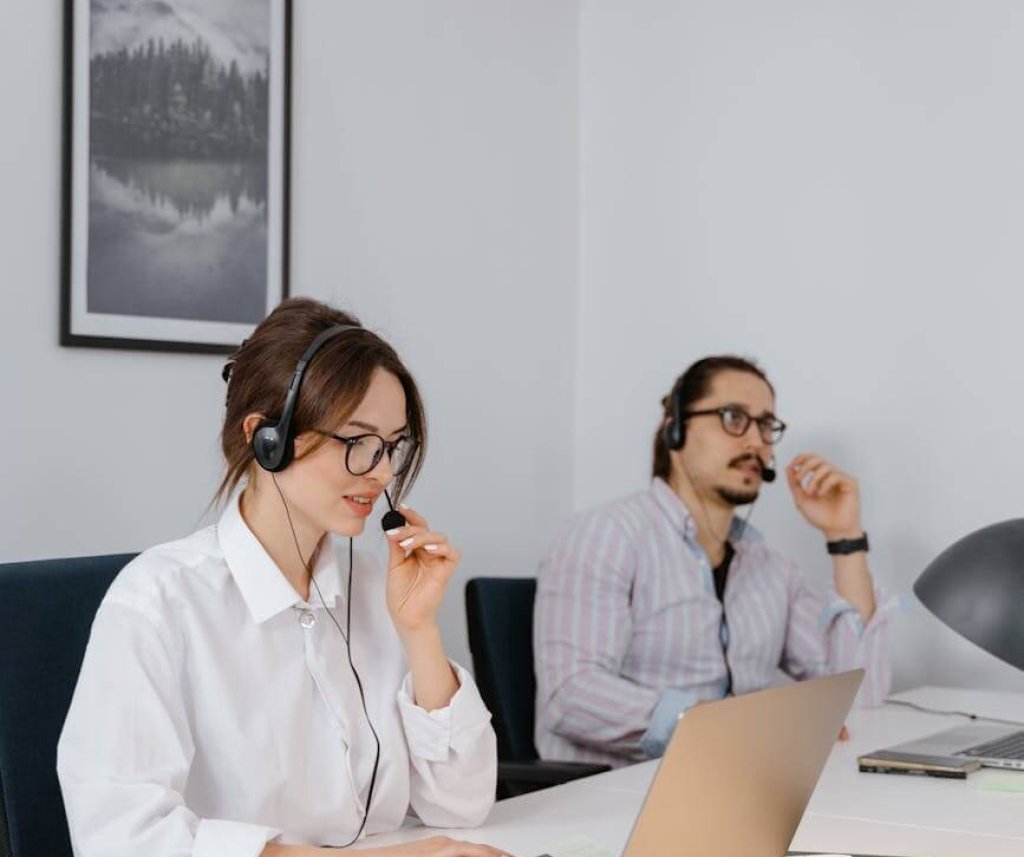 pexels-photo-7709085-7709085 Two professionals working remotely in a modern office space, wearing headsets and using laptops.